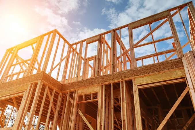 A house under construction, wood framing against a blue sky